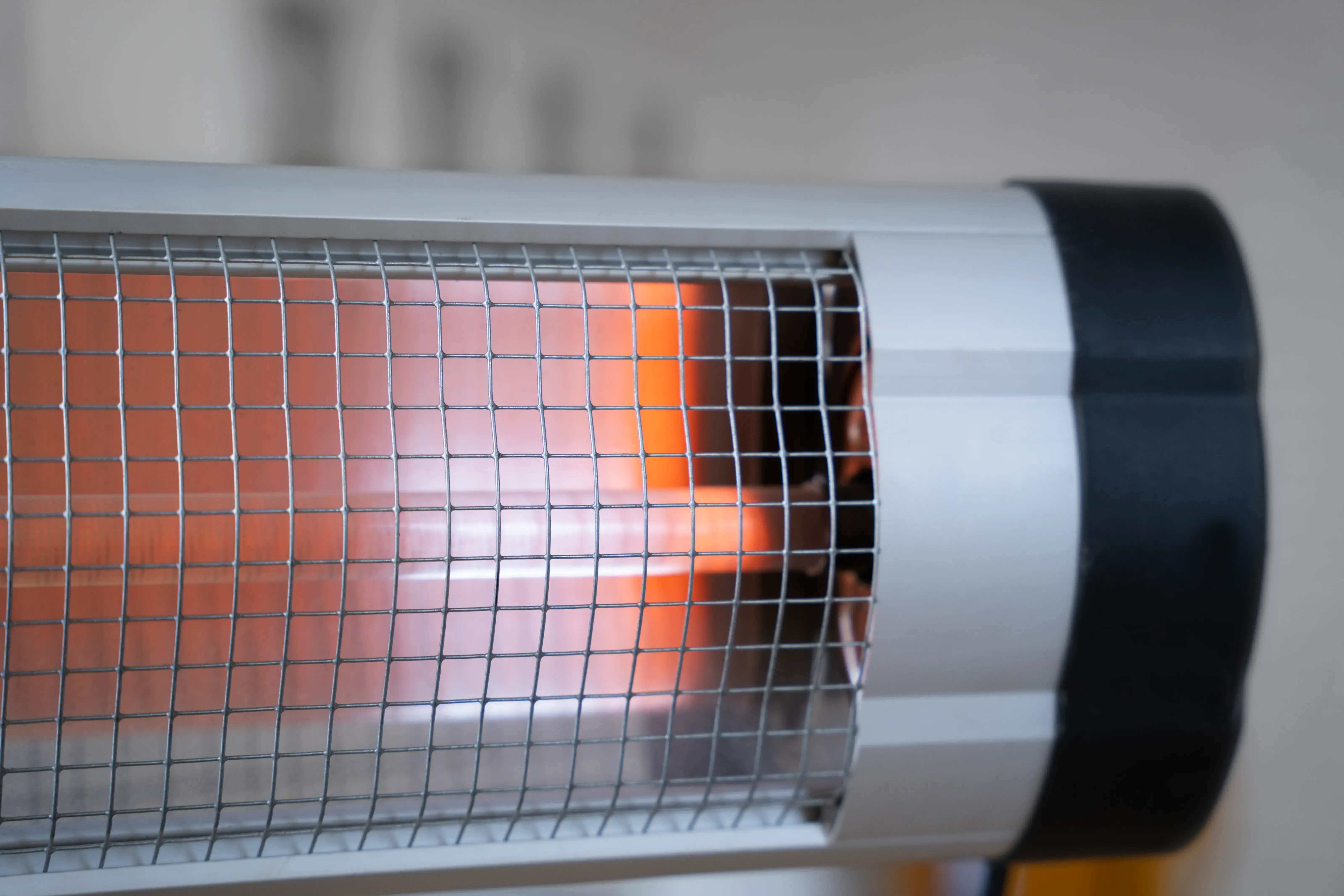 Close-up of a silver electric heater with a wire mesh covering an orange heating element.