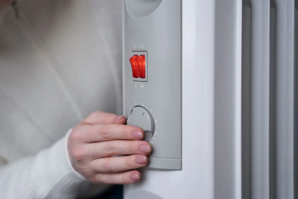 Person adjusting the temperature dial on a white space heater with a red power switch.