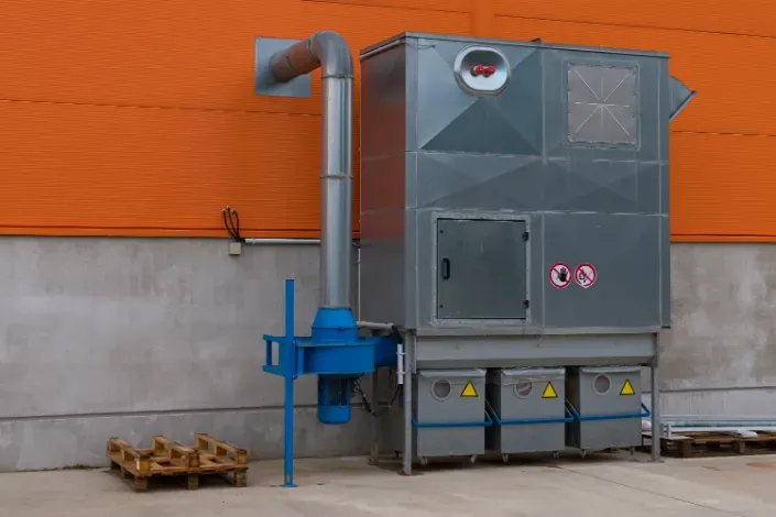 Silver industrial air filtration system outside an orange building, with connected blue fan and ductwork.